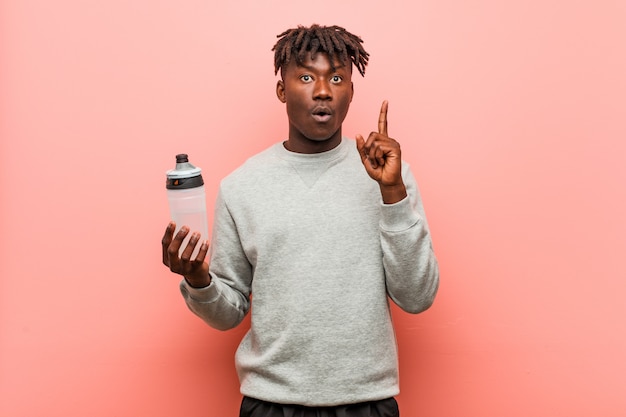 Young fitness black man holding a water bottle impressed holding copy space  on palm. Stock Photo
