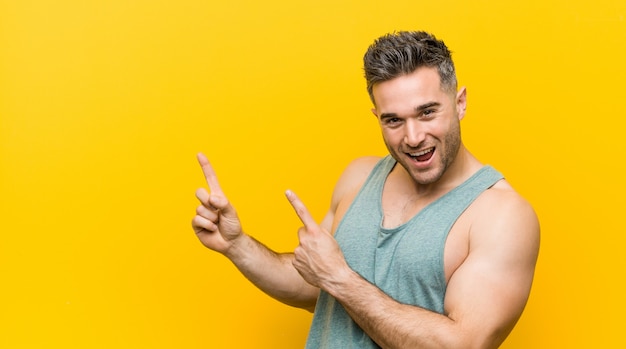 Young fitness man pointing with forefingers to a copy space, expressing excitement and desire.