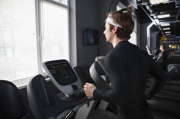 Giovane uomo di forma fisica che corre su un tapis roulant in fase di riscaldamento in palestra