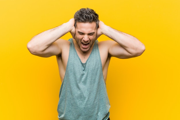 Young fitness man on yellow covering ears with hands trying not to hear too loud sound.