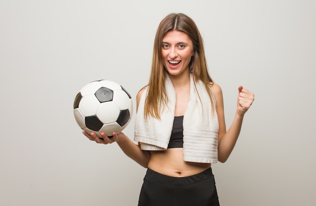 Young fitness russian woman screaming very angry and aggressive. Holding a soccer ball.