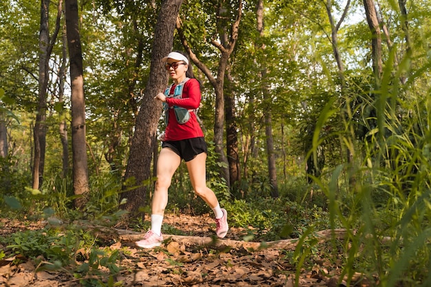 Young fitness sportswoman trail runner running in the tropical forest park in the evening