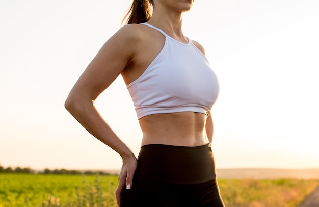 Young fitness sporty woman posing in sports clothing and relaxing after workout. Close up strong abs showing.