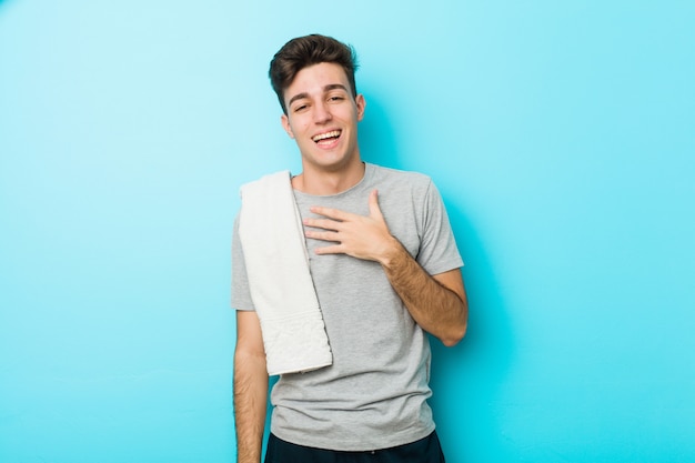 Young fitness teenager man laughs out loudly keeping hand on chest.