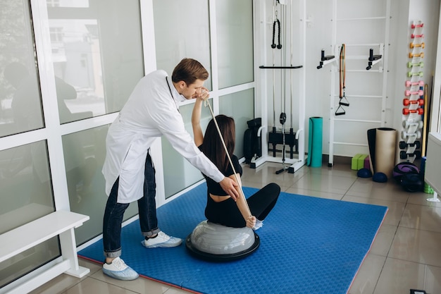 Young fitness woman doing kinesiotherapy rehabilitation exercise with personal rehabilitation specialist in the gym