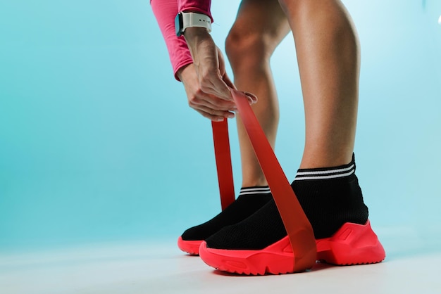 Young fitness woman doing squats with fitness loop band isolated on blue background