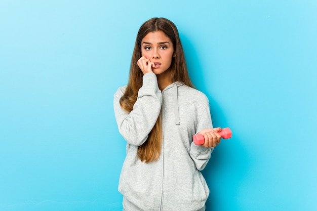 Young fitness woman holding a weight biting fingernails, nervous and very anxious.