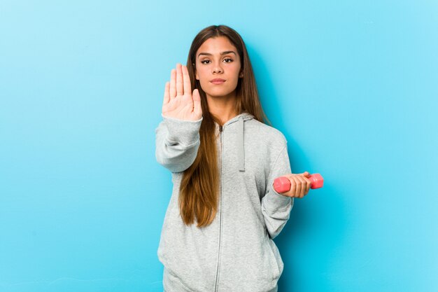 Photo young fitness woman holding a weight standing with outstretched hand showing stop sign, preventing you.