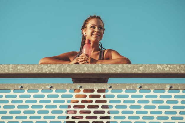 Foto la giovane donna fitness sta riposando dopo un duro allenamento sul ponte sul fiume, ascoltando musica e distogliendo lo sguardo.