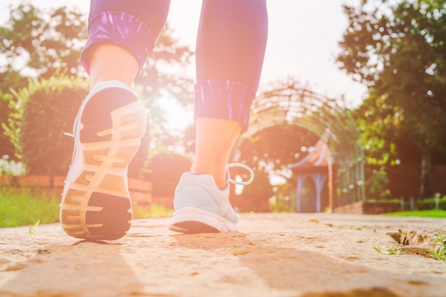 Giovani gambe della donna di forma fisica che camminano di mattina al parco pubblico all'aperto.