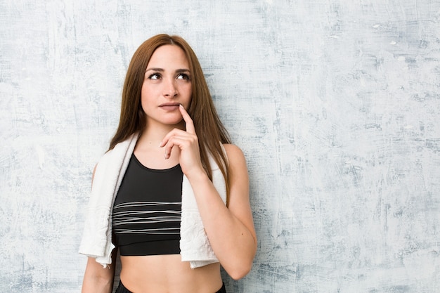 Young fitness woman looking sideways with doubtful and skeptical expression.