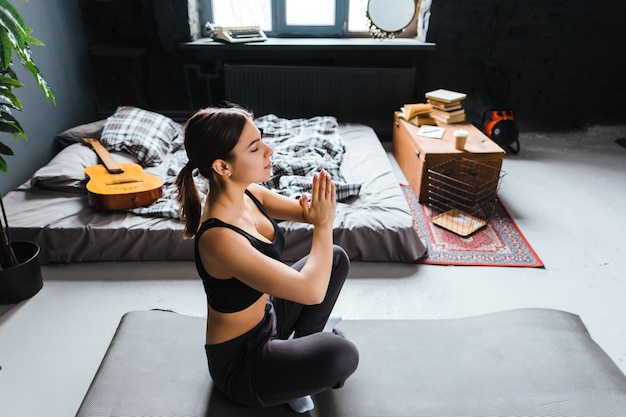 Young fitness woman meditate, doing yoga indoors at home near the bed