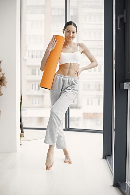 Young fitness woman ready for workout holding orange yoga mat