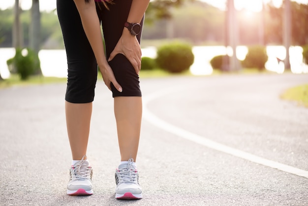 Il giovane corridore della donna di forma fisica sente il dolore sul suo ginocchio nel parco.