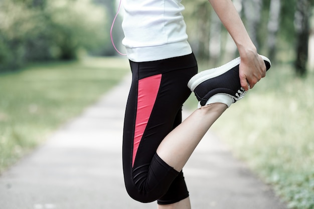 Young fitness woman runner stretching legs before run on grass