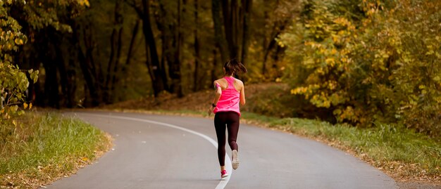 황금빛 가을 숲길을 달리는 젊은 피트니스 여성