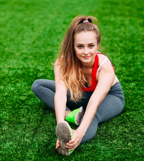 Young fitness woman sitting on green grass .