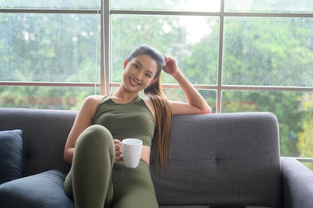 Young fitness woman in sportswear having a cup of coffee after exercising at home