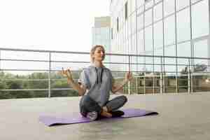 Photo young fitness woman in sportswear practicing yoga, meditates on rooftop of building, urban style