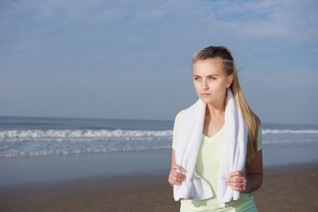 Young fitness woman standing at the beach with towel