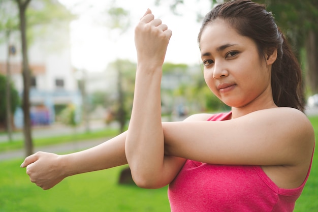 屋外で運動する前に腕、三叉、肩を伸ばしている若いフィットネス女性。