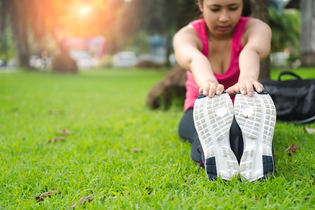 La giovane donna di forma fisica che allunga prima dell'esecuzione e si esercita all'aperto in parco.