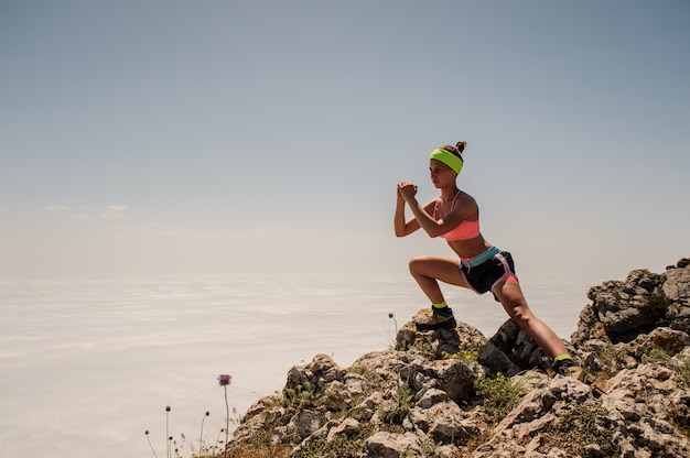 Young fitness woman trail runner tying shoelace at mountain top