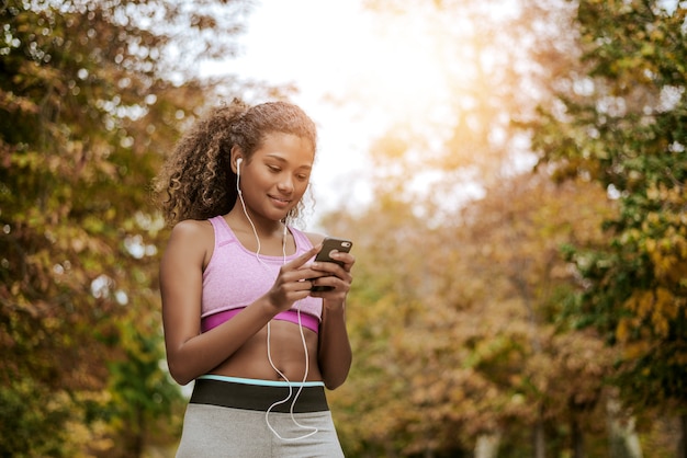 Young fitness woman using phone after running outdoors in park.