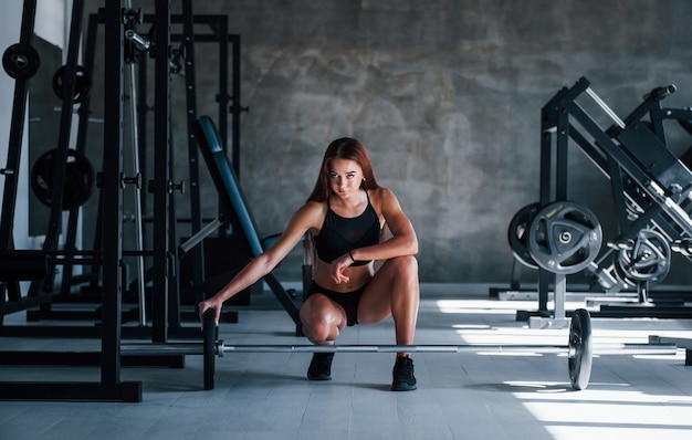 Young fitness woman with slim type of body and in black sportive clothes is in the gym.