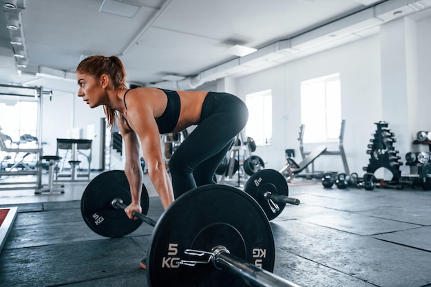 Young fitness woman with slim type of body doing exercises by using barbell