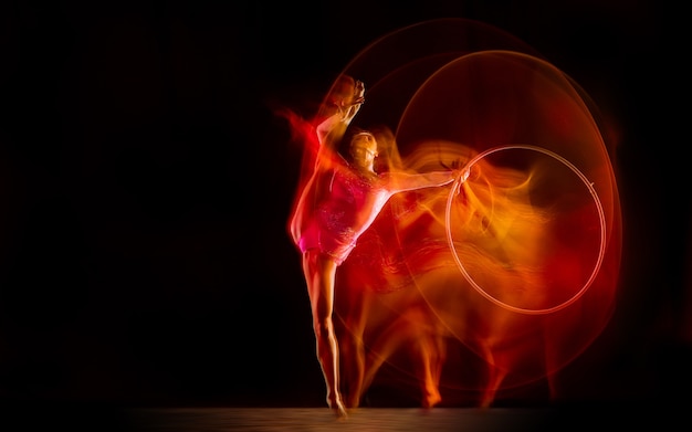 Foto giovane ginnasta femminile flessibile isolata sul fondo nero dello studio nella luce mista