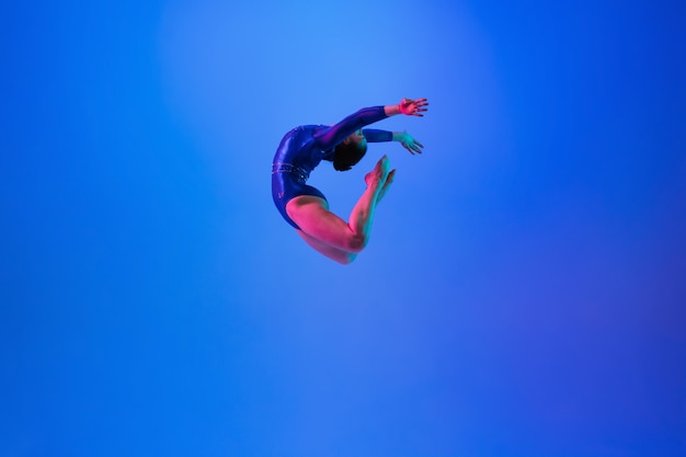 Photo young flexible girl isolated on blue studio background young female model practicing artistic gymnastics exercises for flexibility balance