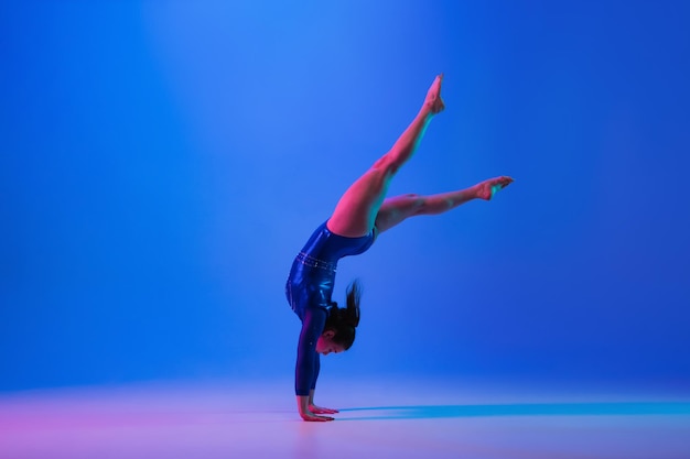 Young flexible girl isolated on blue studio background Young female model practicing artistic gymnastics Exercises for flexibility balance