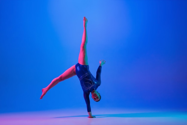 Young flexible girl isolated on blue studio background Young female model practicing artistic gymnastics Exercises for flexibility balance