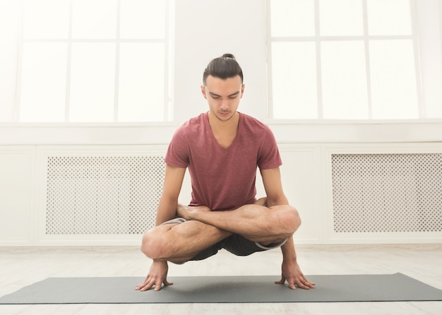 Young flexible man practicing yoga, standing on hands in lotus pose on mat in fitness class, copy space