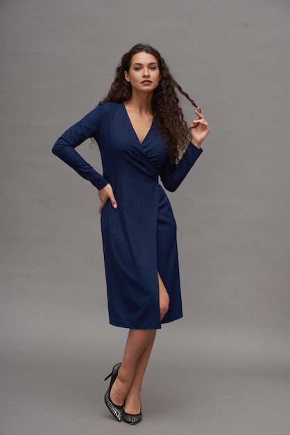 Young flirty woman in blue dress and high heeled shoes posing for camera