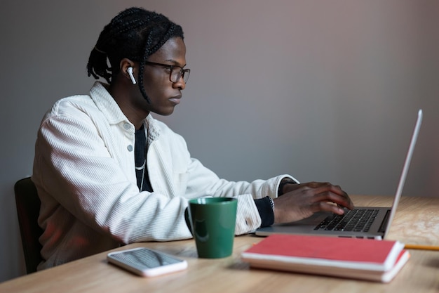 Young focused African American man sits at wooden table with laptop getting internet education