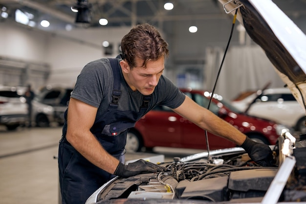 Il giovane maschio americano o caucasico concentrato può aggiustare qualsiasi cosa un bel meccanico di auto in uniforme generale c...