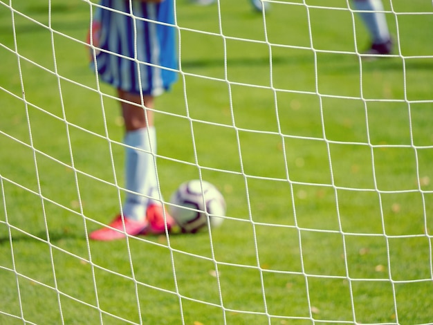 Foto giovane portiere di calcio nel campo di calcio fuori fuoco vista attraverso la rete del cancello di calcio