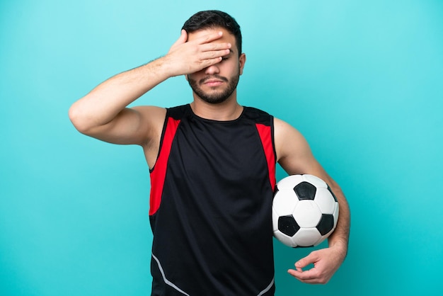 Young football player brazilian man isolated on blue background\
covering eyes by hands do not want to see something