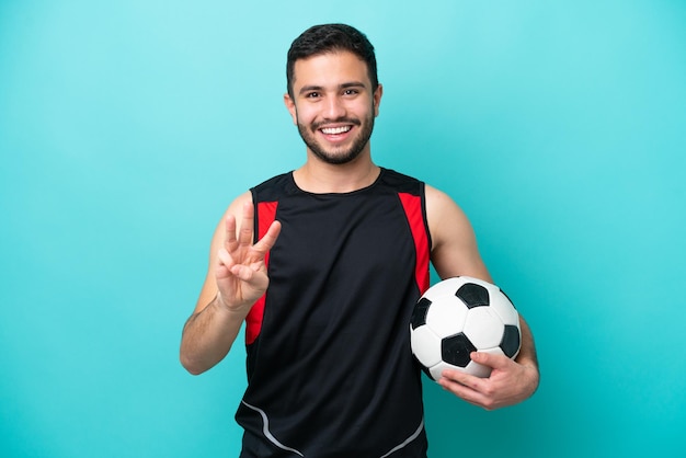 Young football player Brazilian man isolated on blue background happy and counting three with fingers