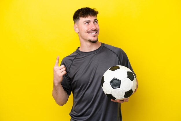 Young football player man isolated on yellow background pointing up a great idea