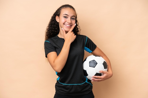 Молодая женщина-футболистка на бежевом фоне счастлива и улыбается