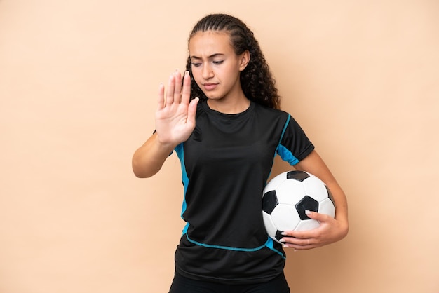 Young football player woman isolated on beige background making\
stop gesture and disappointed