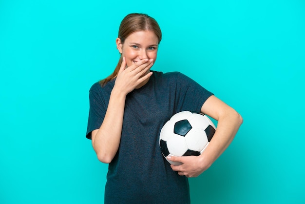 Young football player woman isolated on blue background happy and smiling covering mouth with hand