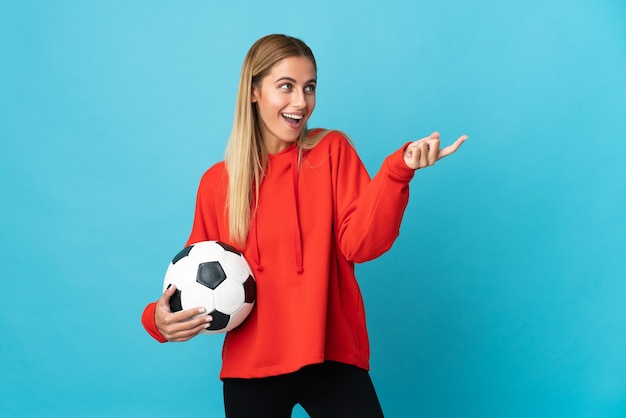 Young football player woman isolated on blue background pointing finger to the side and presenting a product