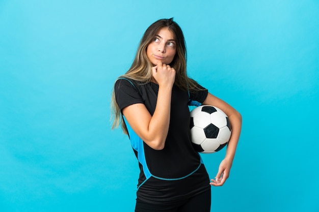 Молодая женщина футболиста изолирована на синем и смотрит вверх