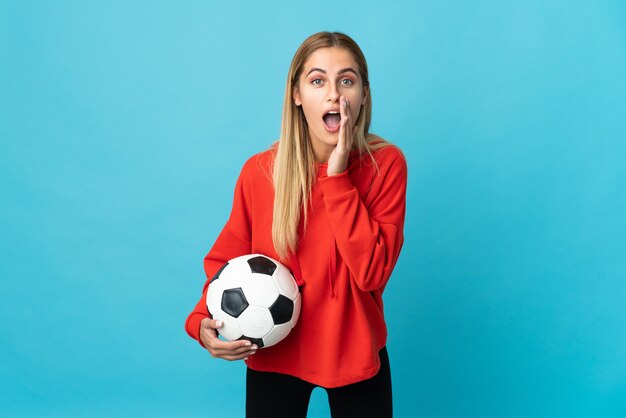 Young football player woman isolated on blue space shouting with mouth wide open