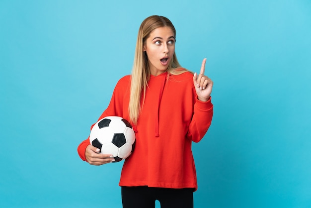 Young football player woman isolated on blue space thinking an idea pointing the finger up