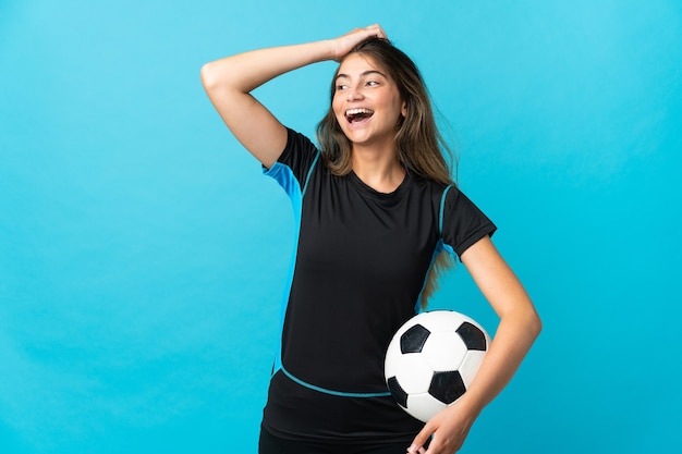 Young football player woman isolated on blue wall smiling a\
lot